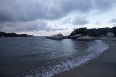 Bulutlu gökyüzü orman dağları ve arka planda büyük kayalarla Kolombiya Tayrona Ulusal Parkı 'nın güzel mavi alacakaranlık sahnesi