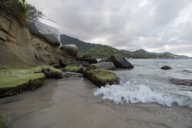 Güzel yosunlu kayalar bulutlu alacakaranlıkta Kolombiya tayrona plajına düşüyor.
