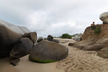 Dağın tepesinde oturmuş, Kolombiya Tayrona Milli Parkı 'na okyanus manzarası seyreden bir kadın.