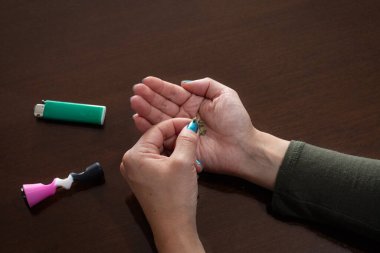 Elinde küçük bir parça esrar tutan genç bir kadın, elinde çakmak ve esrar piposuyla.