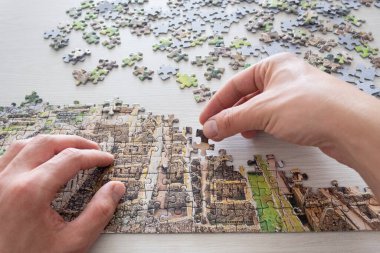 First person view of a male hands solving a jigsaw over a white wooden table at background  clipart