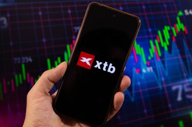 BOGOTA, COLOMBIA - 05 Mart 2025 xtb broker yazılım logosu ve borsa bulanık arkaplan içeren akıllı telefonu tutan bir erkek.