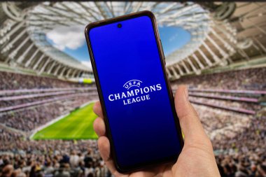 BOGOTA, COLOMBIA - 05 Mart 2025 Uefa Şampiyonlar Ligi logosu ve arka planda bulanık bir futbol stadyumu olan akıllı telefonu elinde tutan bir erkek.