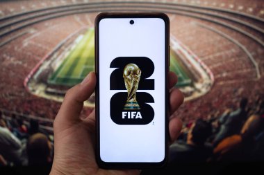 BOGOTA, COLOMBIA - 05 Mart 2025 Beyaz zemin üzerinde Fifa Dünya Kupası 2026 logosu olan akıllı telefon taşıyan bir erkek el arka planda bulanık futbol stadyumu