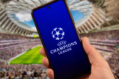 BOGOTA, COLOMBIA - 05 Mart 2025 Uefa Şampiyonlar Ligi logosu ve arka planda bulanık bir futbol stadyumu olan akıllı telefonu tutan bir erkeğe yakın çekim