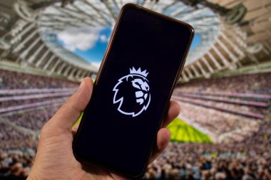 BOGOTA, COLOMBIA - Premier League futbol aslanı sembollü bir akıllı telefon ve arka planda bulanık futbol stadyumu