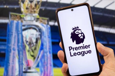 BOGOTA, COLOMBIA - Premier League futbol ligi aslan logosuna sahip bir akıllı telefon ve arka planda bulanık bir Premier Lig kupası