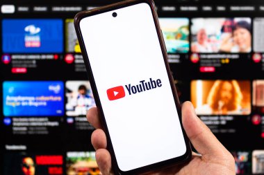 BOGOTA, COLOMBIA - 05 Mart 2025 Bir erkek sağ eliyle akıllı telefon tutuyor ve Youtube logosu arka planda bulanık youtube arayüzü var