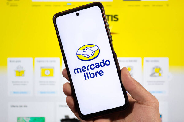 BOGOTA, COLOMBIA - MARCH 05 OF 2025 closeup to a male hand with mercado libre logo inside a smartphone with mercado libre interface at background