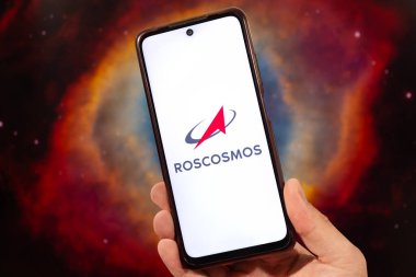 Roscosmos logosu ve arka planda bulanık bir nebula olan akıllı telefonu tutan bir erkek el.