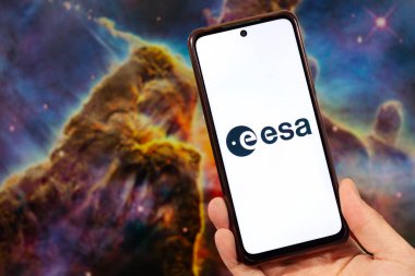 ESA logosu ve arka planda bulanık bir uzay görüntüsü olan akıllı telefonu tutan bir erkek el.