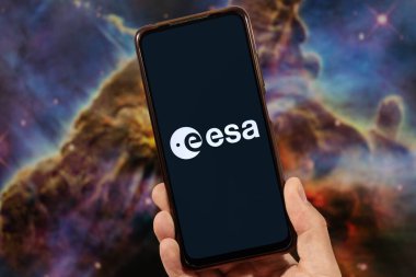 Sağ eliyle akıllı telefon tutan bir erkek ve arka planında bulanık uzay görüntüsü olan Avrupa Uzay Ajansı logosu.