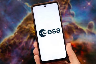 Üzerinde Avrupa Uzay Ajansı logosu olan ve arka planda bulanık uzay görüntüsü olan bir akıllı telefon tutan bir erkek.