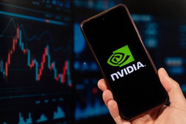 Nvidia şirketinin logosu ve arka planda bulanık bir borsa konsepti olan akıllı telefonu elinde tutan bir erkek.