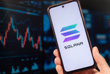  Solana şirketinin logosuna sahip akıllı telefonu olan bir erkek ve arka planda bulanık bir borsa konsepti.