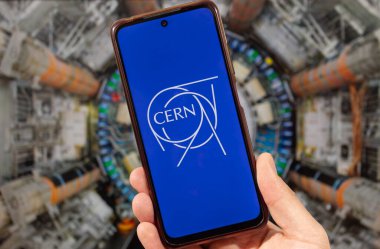 Sağ eliyle akıllı telefonu tutan bir erkek ve arkasında bulanık bir Hadron Çarpıştırıcısı bulunan Avrupa Nükleer Araştırma Örgütü logosu.