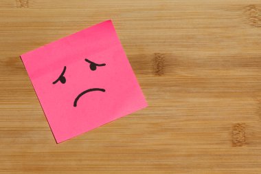 Yapışkan bir nota yakın, sol tarafında hüzünlü bir yüz olan tahta bir arka planda.