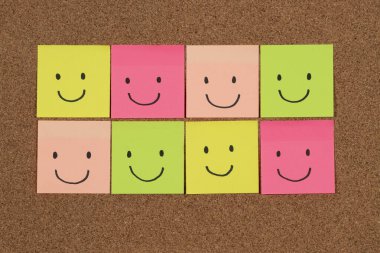 Bir mantar arkaplan üzerinde bir sürü mutlu yüzü temsil eden çok renkli yapışkan notlar grubuna yaklaş