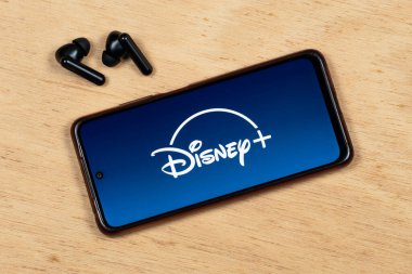 Mavi gradyan ve beyaz disneyli akıllı telefonlu kablosuz kulaklıklara yakın dur. Ayrıca tahta arka planda bir logo var.