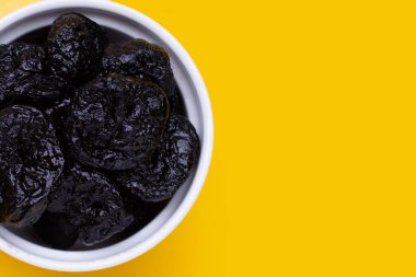 Dried prunes on yellow background