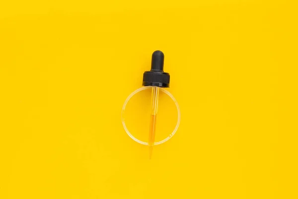 Essential oil in dropper on yellow background.