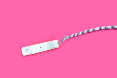 Handset of landline phone on pink background.