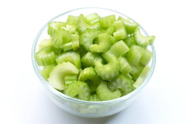 Fresh celery slices in glass bowl on white background. 