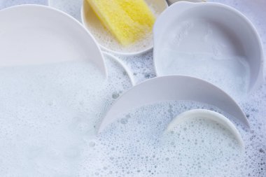 Dishes and bowls with yellow sponge in water and bubbles of dishwashing liquid