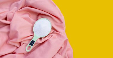 Detergent powder in measuring spoon on cloth before washing. Laundry concept.