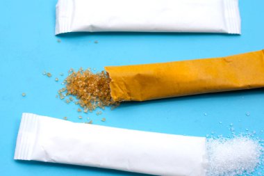 Mavi arkaplanda beyaz ve kahverengi şeker kesesi.