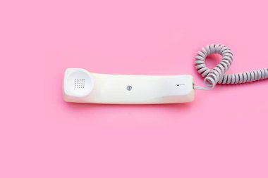 Handset of landline phone on pink background.