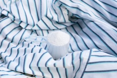 Detergent powder in measuring spoon on cloth before washing. Laundry concept.