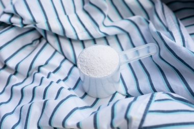 Detergent powder in measuring spoon on cloth before washing. Laundry concept.