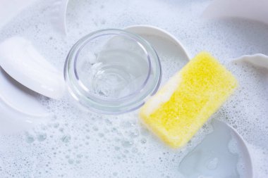 Dishes and bowls with yellow sponge in water and bubbles of dishwashing liquid