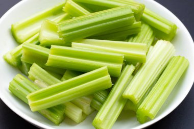 Koyu arkaplanda beyaz tabakta taze kereviz. 