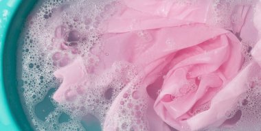 Giysiler toz deterjana batırılmış. Su çözünmüş, renkli giysiler yıkanmış.