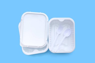 Mavi arka planda çatal ve kaşıkla plastik yiyecek kutuları..
