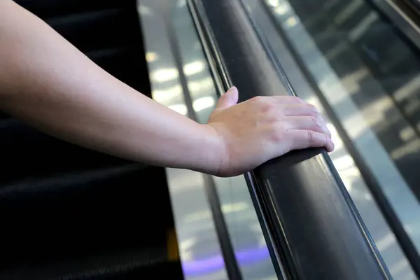 Hand holding escalator handrail in shopping mall or building