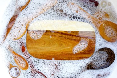 Su içinde ahşap mutfak eşyaları ve bulaşık deterjanı köpükleri.