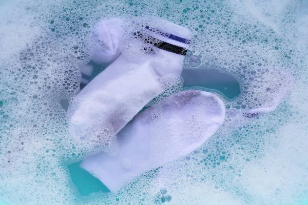 Dirty white socks soaked in water, dissolving detergent in blue basin.