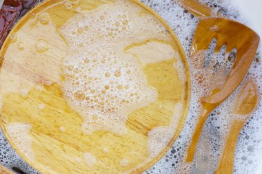 Su içinde ahşap mutfak eşyaları ve bulaşık deterjanı köpükleri.