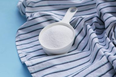 Detergent powder in measuring spoon on cloth before washing. Laundry concept.
