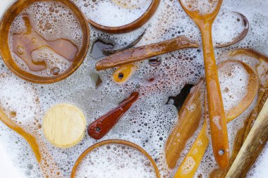 Su içinde ahşap mutfak eşyaları ve bulaşık deterjanı köpükleri.