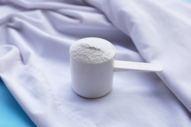 Detergent powder in measuring spoon on cloth before washing. Laundry concept.