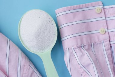 Detergent powder in measuring spoon on cloth before washing. Laundry concept.