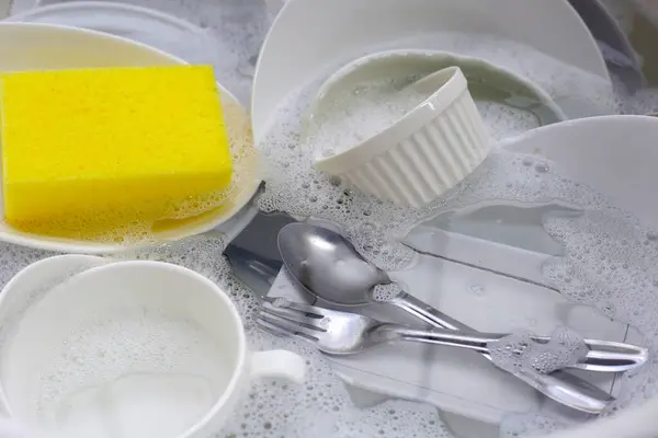 Dirty dishes with cleaning sponge in foam of dishwashing liquid. Washing dishes concept