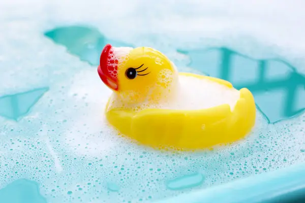 Yellow duck rubber toy with foam bubbles in blue basin