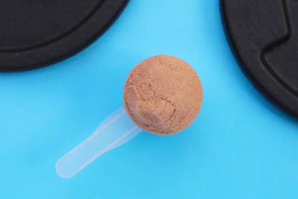Whey protein powder with iron weight plates on blue background.