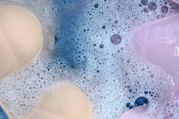 Beyaz köpüklü, çözünmüş deterjana batırılmış kadın sütyeni. Çamaşır konsepti