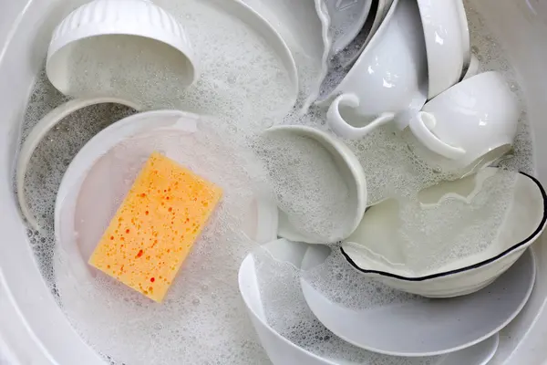 Dirty dishes with cleaning sponge in foam of dishwashing liquid. Washing dishes concept